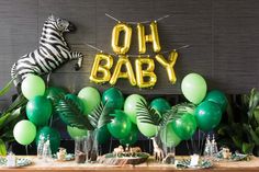 a table topped with balloons and jungle themed desserts next to a zebra balloon sign