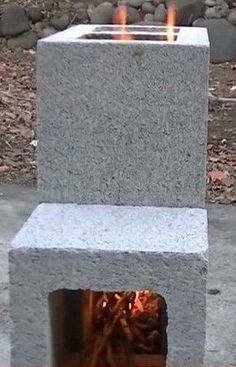 a fire pit made out of concrete blocks with flames burning in the center and rocks surrounding it