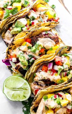 several tacos are lined up on a white plate with lime wedges and cilantro