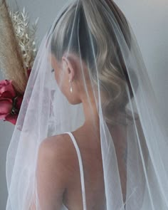 a woman wearing a wedding veil and holding a flower in her left hand, looking down at the ground