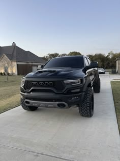 a black truck parked on top of a cement driveway next to a house and trees