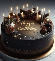 a chocolate birthday cake with lit candles on it's top and the words happy birthday written in gold