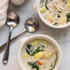 two bowls of chicken and vegetable soup on a table with spoons next to it