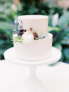 a white wedding cake with flowers and greenery on top is sitting on a table