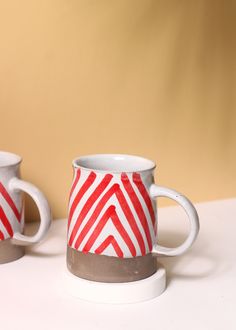 two red and white coffee mugs sitting next to each other on top of a table