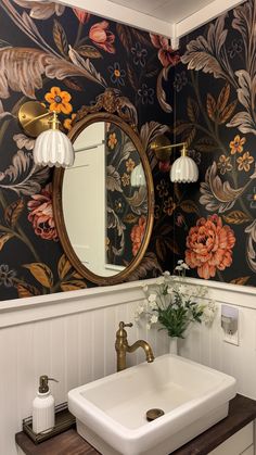 a white sink sitting under a bathroom mirror next to a wooden counter top with flowers on it