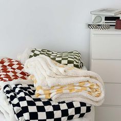 several blankets stacked on top of each other in a room with white walls and drawers