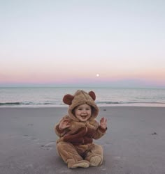 a baby in a bear costume sitting on the beach