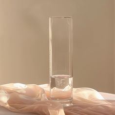 a clear vase sitting on top of a table next to a white cloth covered wall