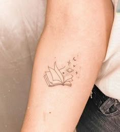 a woman's arm with a book and stars tattoo on the left side of her arm