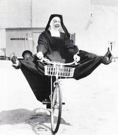 an old photo of a nun riding a bike with her legs spread out in the air