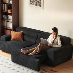 a woman sitting on top of a couch using a laptop computer next to a book shelf