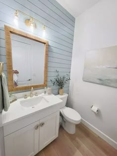 a white bathroom with wood flooring and blue wallpaper on the walls, along with a wooden framed mirror