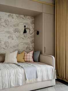 a day bed with pillows on it in front of a wallpapered closet and window