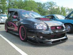 a black car with pink rims parked in a parking lot next to other cars