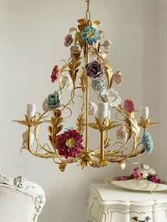 an ornate chandelier with flowers on it in a white room next to a chair