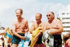 three men standing next to each other at the beach with towels on their shoulders and one holding a towel