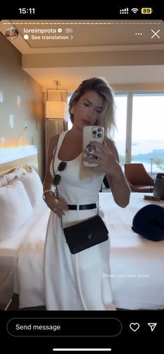 a woman taking a selfie with her cell phone in front of the camera, wearing a white dress