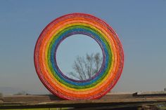 a rainbow colored circular mirror sitting on top of a wooden fence