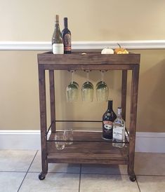 a wooden bar cart with three wine glasses and bottles on the top, sitting in front of a wall