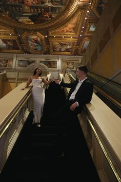 a man and woman standing on an escalator in a building with paintings on the ceiling