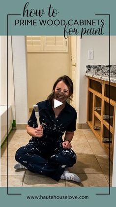 a woman sitting on the floor in front of a cabinet holding a paintbrush and smiling