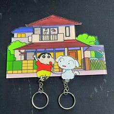 two key chains with cartoon characters attached to them on a black surface next to a house