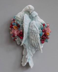 an angel statue with flowers and berries on it's back end, against a gray background