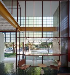 an empty room with chairs and tables in front of glass walls that look like they have been partitioned from the outside