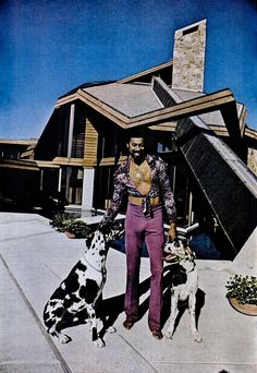 a man standing next to two dogs in front of a house