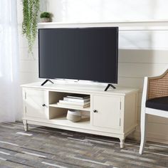 a flat screen tv sitting on top of a white entertainment center next to a chair