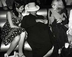 black and white photograph of three women sitting on a couch talking to each other with people in the background