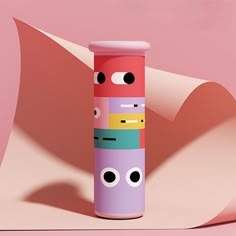 a tall cylindrical tube with eyes and mouth painted on it's side, sitting in front of a pink background