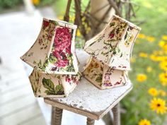 two lamp shades sitting on top of a table next to yellow and pink flowers in a garden