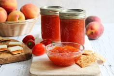 two jars of peach jam sit on a cutting board with crackers and tomatoes in the background