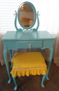 a blue vanity with a mirror and yellow cushion on it's seat in front of a window