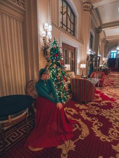 a woman in a long red dress sitting next to a christmas tree with presents on it