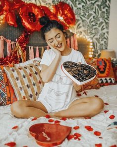 a woman sitting on a bed holding a tray of donuts in front of her face