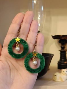 a pair of green earrings with stars and pearls on them are being held up by someone's hand