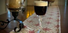 a glass of beer sitting on top of a table next to a candle holder with a lit candle in it