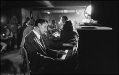 a man sitting at a piano in front of a group of people eating and drinking