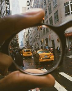 a person's hand holding up a magnifying glass over a city street