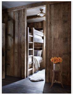 a room with wooden walls and bunk beds in the corner, next to a small table with flowers on it