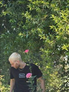 a man in black shirt standing next to a pink flower and green leaves covered tree