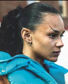 a close up of a person wearing ear piercings and a blue jacket with a brick building in the background