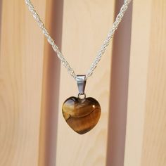 Necklace With Real Polished Stone Pendant On A 18" Silver Metal Chain. The Pendant Is A Polished Gold Tiger's Eye Gemstone In A Heart Shape. Tiger's Eye Is A Beautiful Natural Gemstone Which Glimmers With Gold, Brown And Bronze Highlights. The Pendant Itself Is About 0.5 Inch In Size And Is A Heart Shape. Each Necklace Comes With A Pretty Jewelry Bag To Protect It. This Would Be A Lovely Mother's Day Gift! Tiger's-Eye Gets Its Name Because Of The Reflections Of Light Forming Bands Across The Sto Tigers Eye Crystal Necklace, Tiger Eye Pendant, Silver Gemstone Heart Pendant Necklace, Silver Gemstone Double Heart Necklace, Silver Double Heart Gemstone Necklace, Heart-shaped Sterling Silver Gemstone Necklace, Sterling Silver Heart-shaped Gemstone Necklace, Silver Heart Cut Birthstone Necklace, Silver Sterling Silver Heart Crystal Necklaces