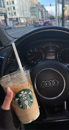 a person holding a drink in their hand next to a car steering wheel and dashboard