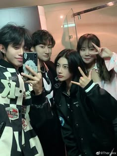 group of young men standing next to each other in front of a mirror taking pictures with their cell phones