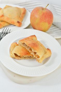 two white plates topped with pastries next to an apple