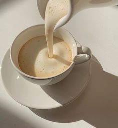 milk being poured into a cup on a saucer